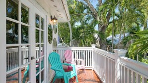 A covered porch with a white railing, two turquoise Adirondack chairs, and a small table. - Monkey House by Avantstay Pool, by Duval Street (Key West)