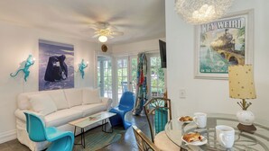 A living room with a white sofa, blue chairs, a glass table with pastries, and a ceiling fan. - Monkey House by Avantstay Pool, by Duval Street (Key West)