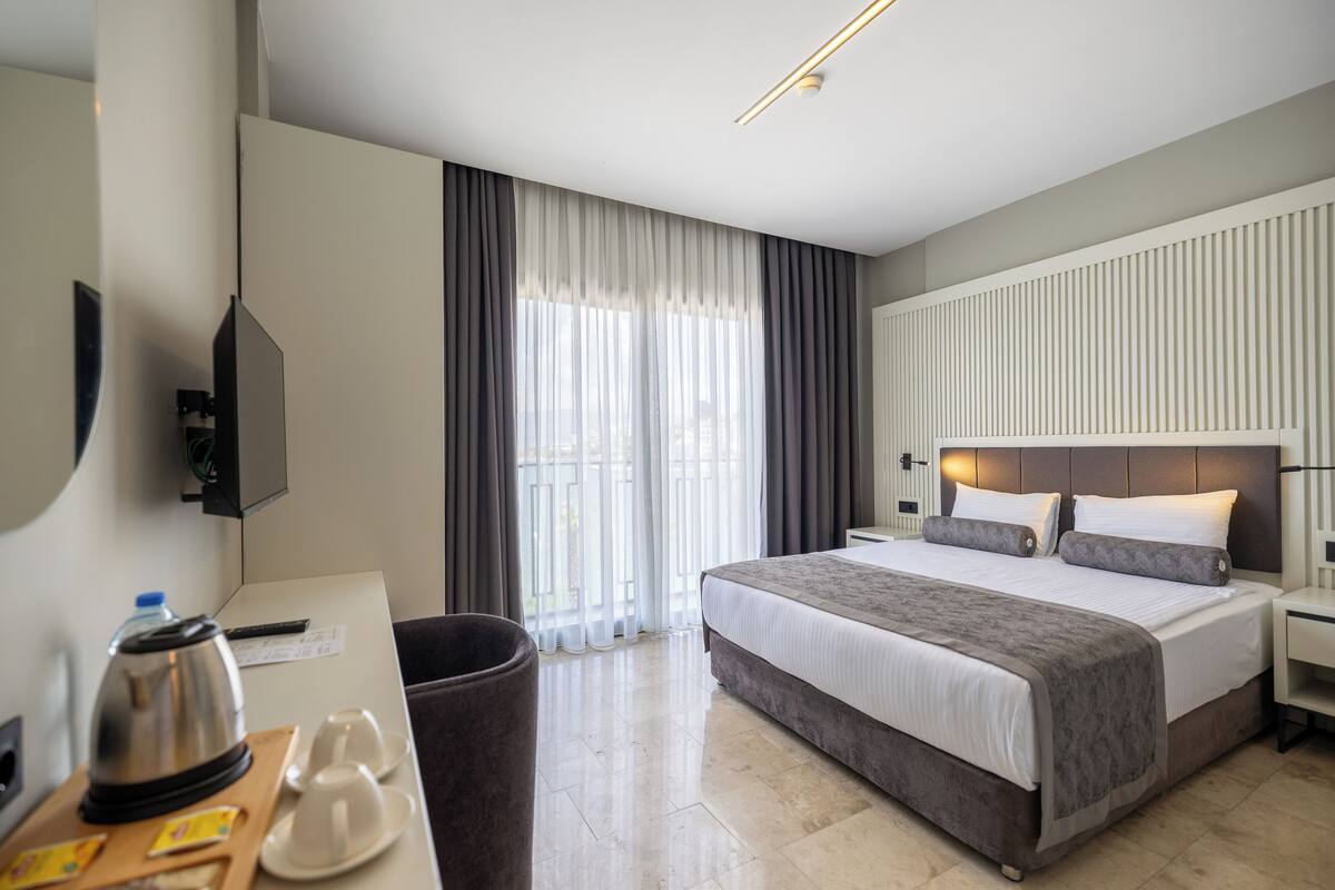Hotellihuone, jossa on sänky, yöpöytä ja työpöytä, sekä vedenkeitin ja kuppeja.