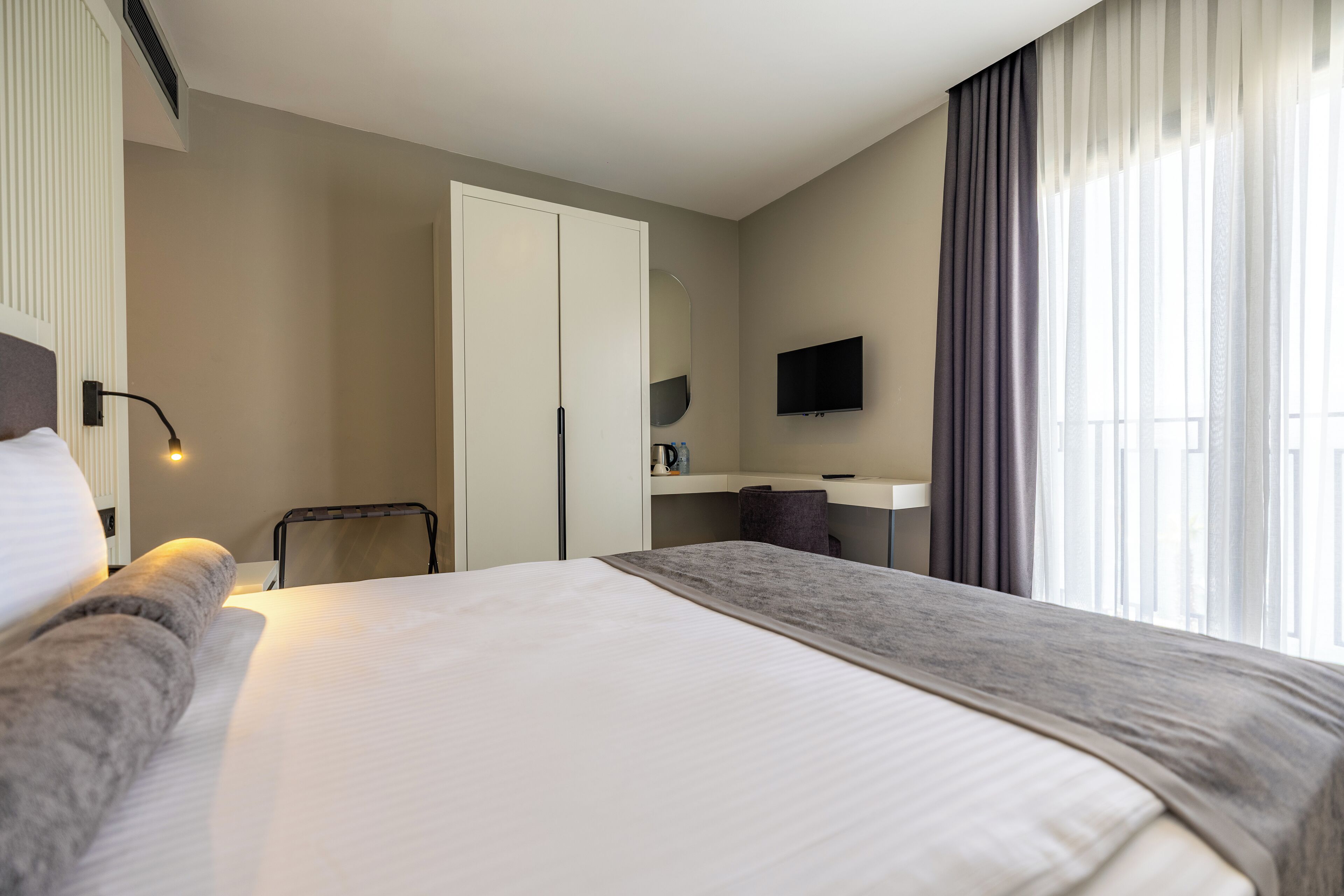 A hotel room with a large bed, a desk, a chair, a TV, and a window with curtains.