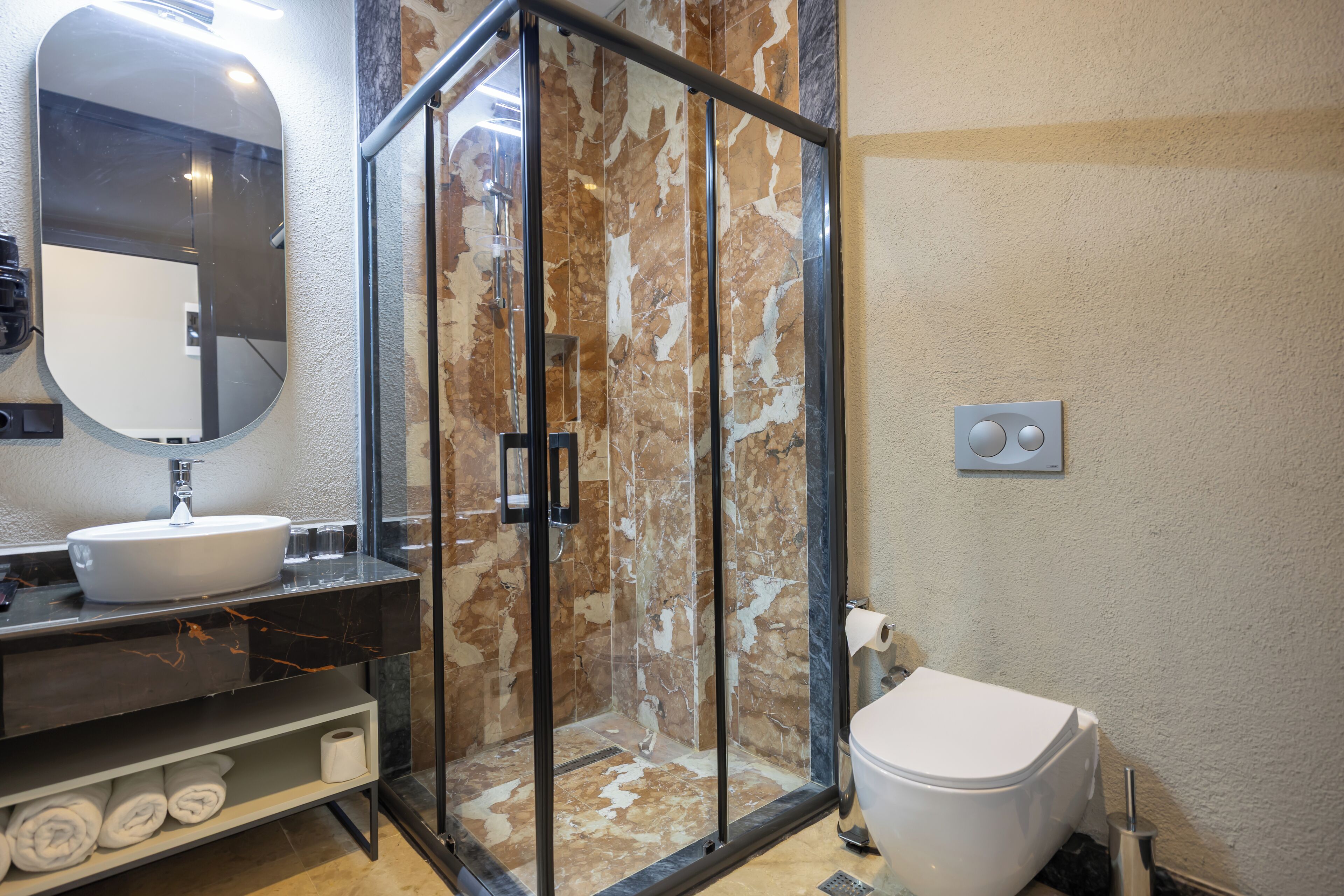 Un baño moderno con ducha de vidrio, un lavamanos blanco y un inodoro.