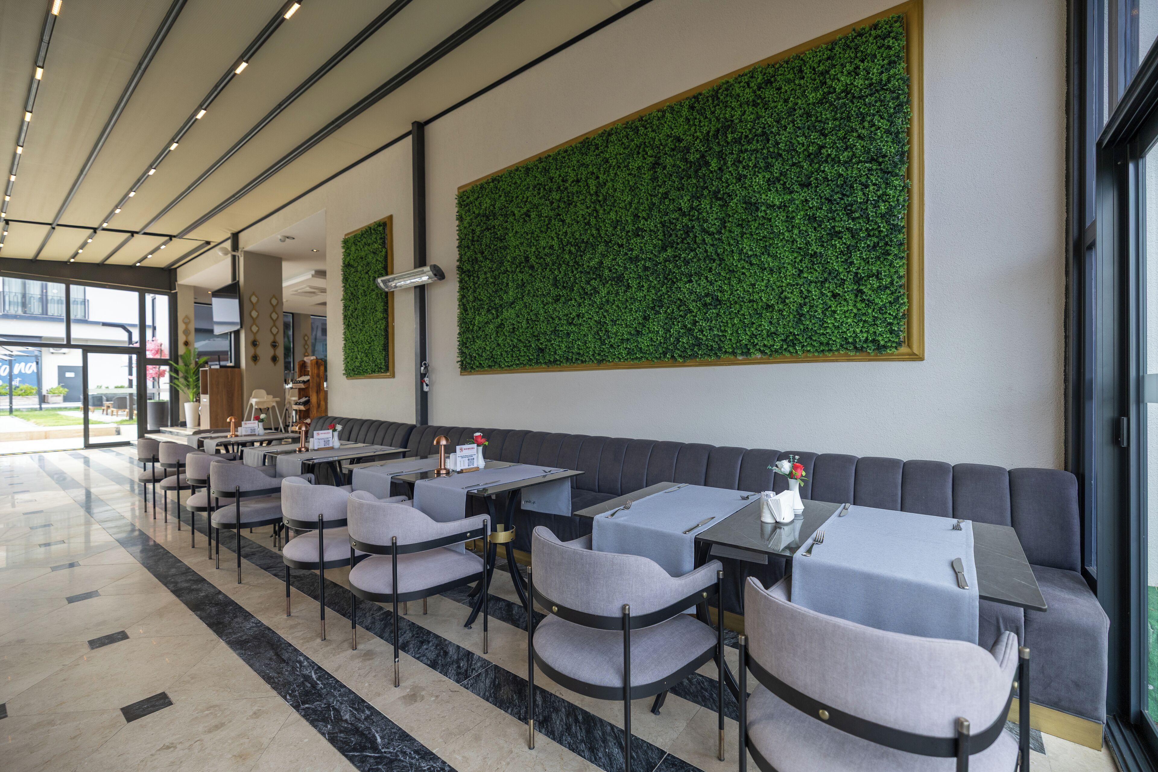 Un restaurante moderno con una barra larga, diversas opciones de asientos, incluyendo un sofá y sillas, y una pared decorativa verde.
