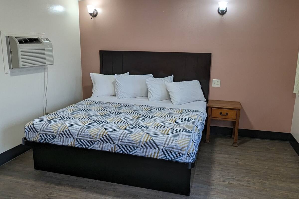 Une chambre à coucher comprenant un lit, une table de chevet, un climatiseur fixé au mur et un luminaire au plafond.