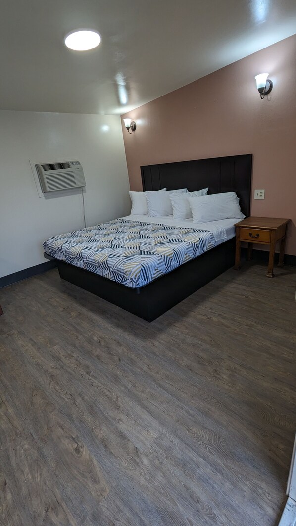 A bedroom with a bed, a nightstand, a wall-mounted air conditioner, and a ceiling light.