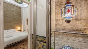 A hotel room with a bed, a patterned floor, a stone wall, and a hanging lantern. - Purasevilla Apartments. Casa Señorial Sevillana (Sevilla)