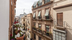 A narrow street with buildings on either side, featuring balconies with potted plants and flower boxes. - Purasevilla Apartments. Casa Señorial Sevillana (Sevilla)