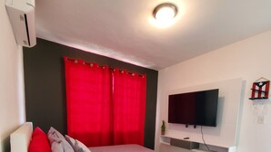 A modern bedroom with a bed, red curtains, a mounted TV, and a small shelf with glasses. - Casa Bird Cage in Fajardo's Paradise, a rainforest like retreat! (fajardo)