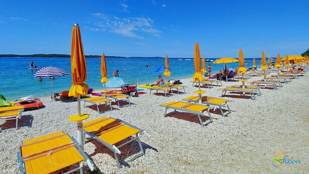 A beach with rows of sun loungers and umbrellas, some occupied by people, and a clear blue sky. - Apartment Ivana - Sea View, Pet Friendly (Fažana)