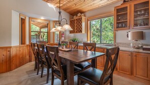 Une cuisine aux murs lambrissés, avec une table et des chaises, de grandes fenêtres et des armoires en bois.