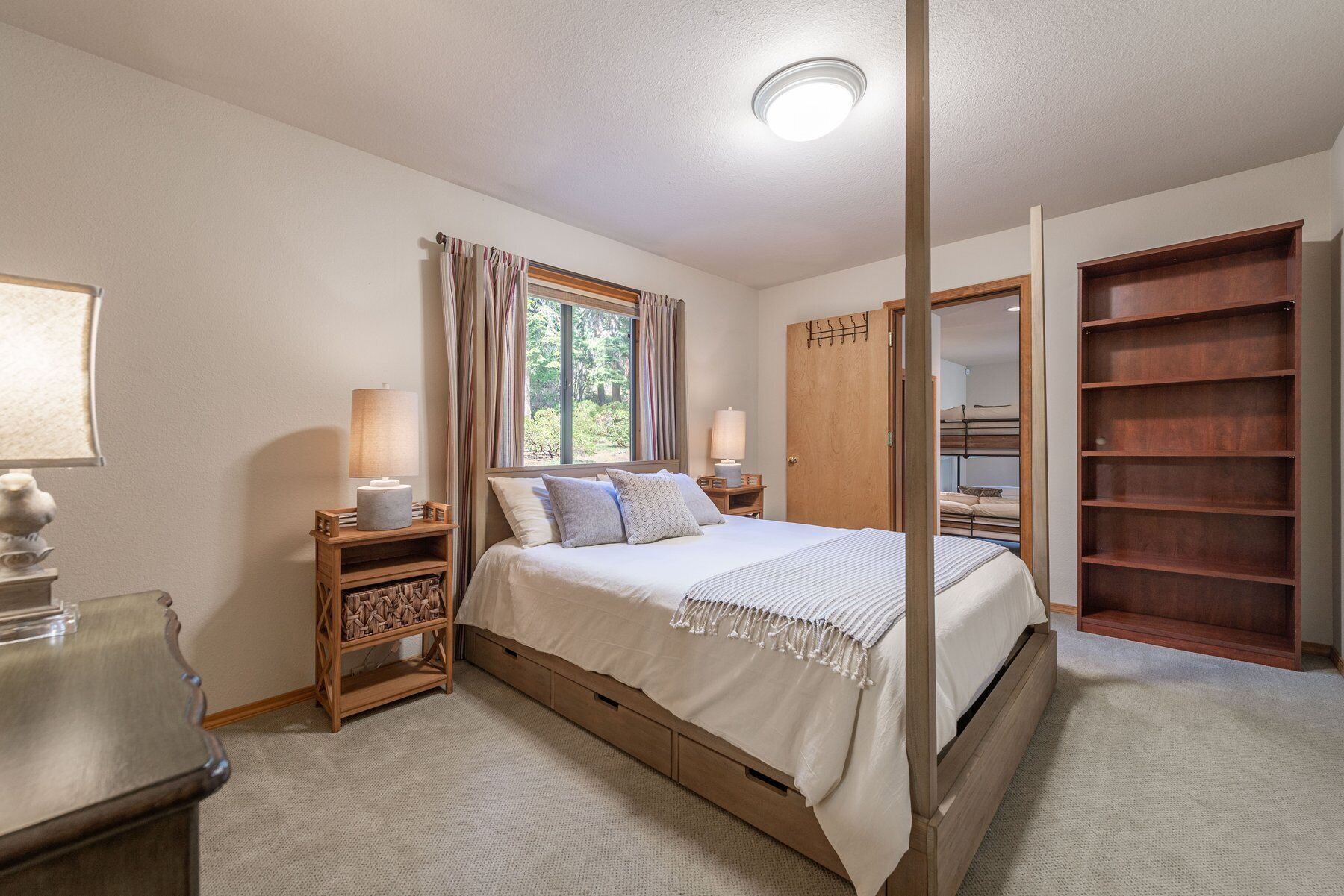 Een slaapkamer met een bed, bedlampen, een raam met gordijnen, een houten garderobe en een inbouwkast.