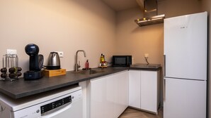 Moderni keittiö, jossa on valkoiset kaapit, musta työtaso, kahvinkeitin, vedenkeitin, mikroaaltouuni ja astianpesukone.
