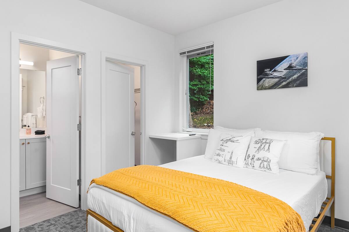 Quarto com cama, janela com vista para vegetação e um quadro na parede.