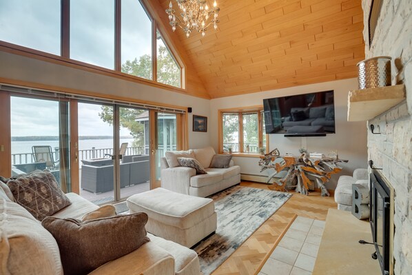 A spacious living room with a large window, a fireplace, and a television. - Pelican Lake House w/ Boat Dock and Sauna! (Pelican Lake)