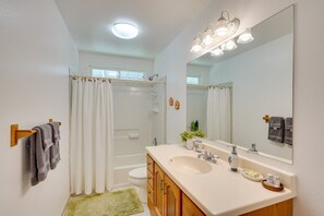 Une salle de bain avec un lavabo blanc, des meubles en bois, un grand miroir et un rideau de douche.