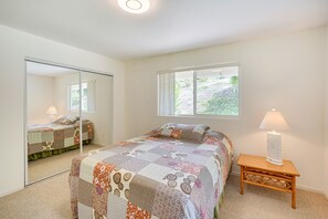 Une chambre avec un grand miroir, un lit recouvert d’une courtepointe à motifs, une lampe de chevet et une fenêtre donnant sur un paysage verdoyant.