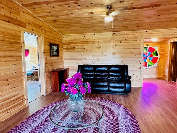 A wooden interior with a black leather sofa, a glass coffee table with a vase of flowers, and a dartboard on the wall. - Boone, ASU, Views, Firepit, HUGE Jac tub, Foosball (Boone)