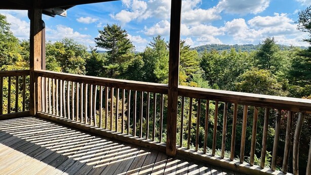 Eine Holzterrasse mit Geländer, die auf einen bewaldeten Bereich unter klarem Himmel blickt.
