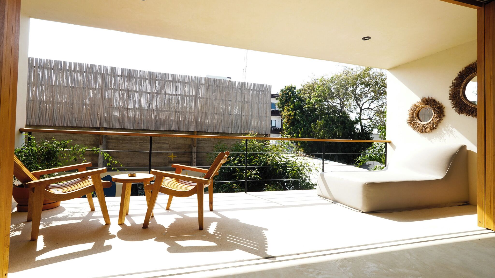 A modern balcony with a sofa, two wooden chairs, and a small table.