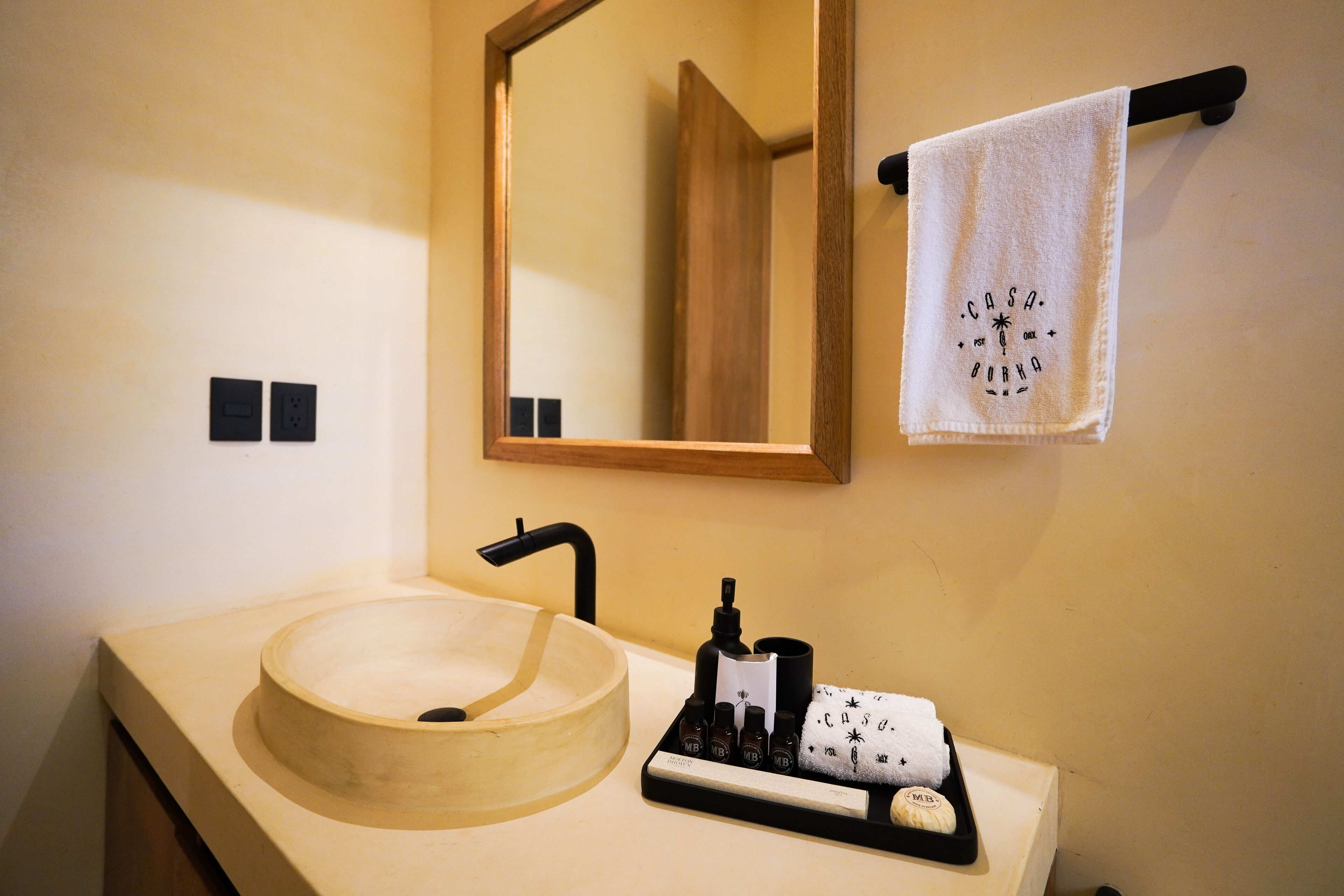 A bathroom with a wooden sink, a black faucet, a mirror, and a towel rack with a white towel.