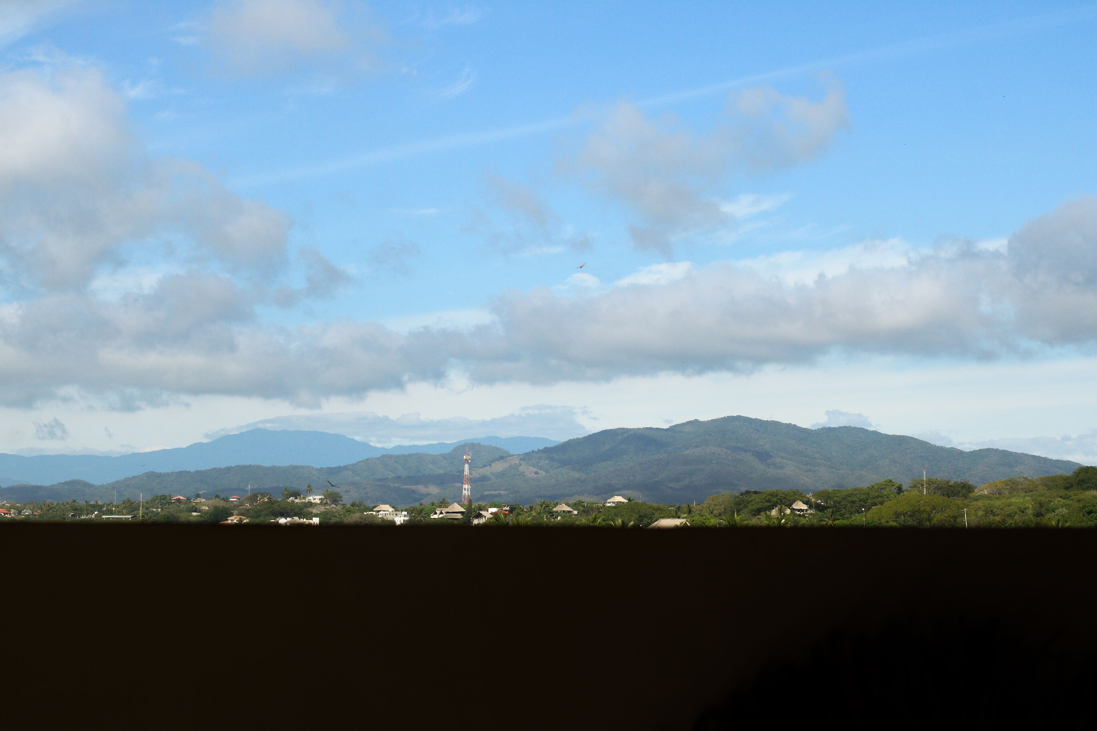 Un paisaje con montañas, una torre y casas dispersas.