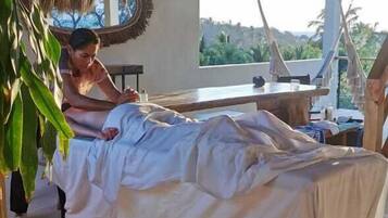Relax in a serene space with a comfortable bed, a large mirror, and a ceiling fan above, surrounded by a thatched roof and natural light.