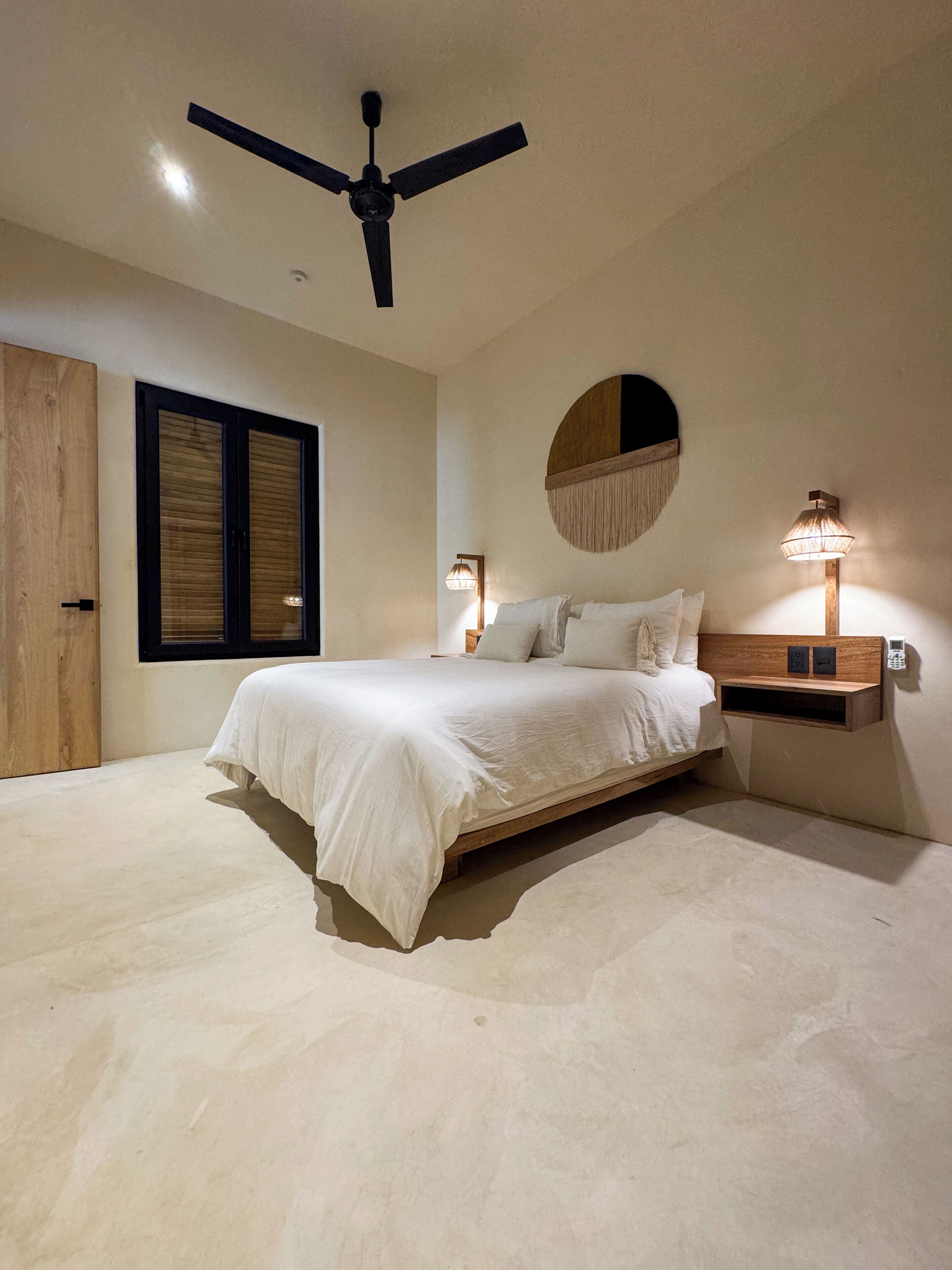 A bedroom with a bed, ceiling fan, wall-mounted lamps, and a wooden door.