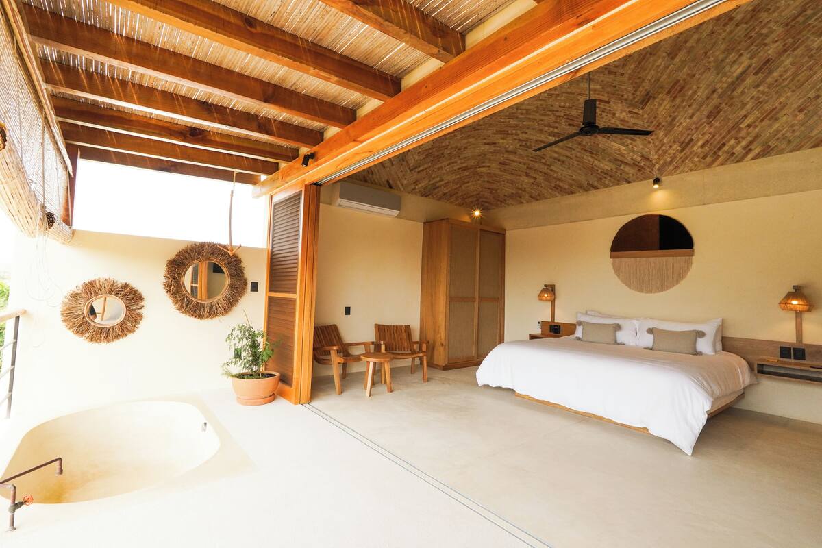 Une chambre spacieuse avec un grand lit, un ventilateur de plafond et une vue sur l’extérieur.