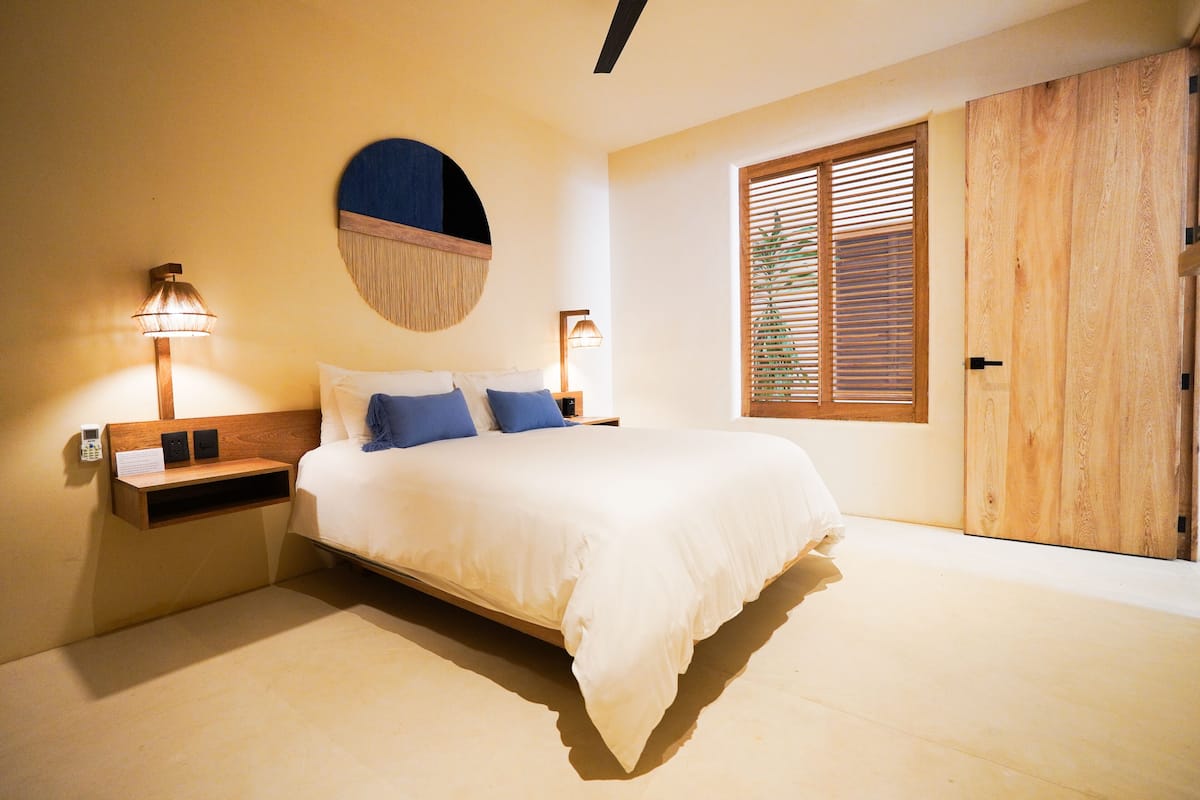 Une chambre à coucher avec un lit, des lampes de chevet, une tête de lit en bois, un miroir rond et une armoire en bois.