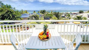Ein Balkon mit Tisch, gedeckt für einen tropischen Fruchtsaft, mit Blick auf einen Strand und einen Parkplatz.