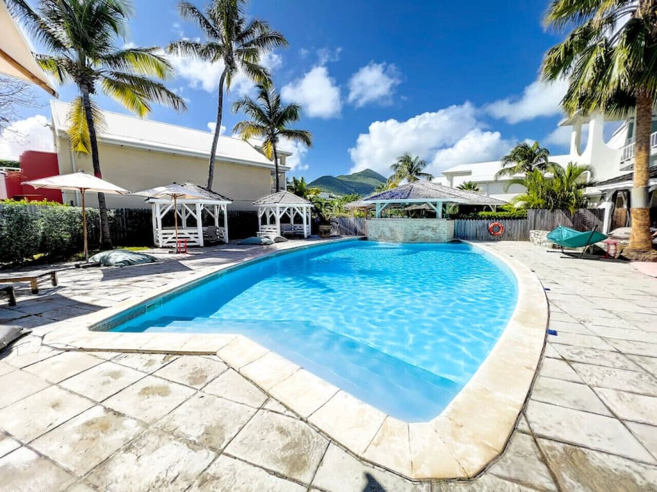 A swimming pool with a tiled deck, palm trees, and a clear blue sky.