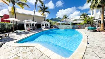 A swimming pool with a tiled deck, palm trees, and a clear blue sky.