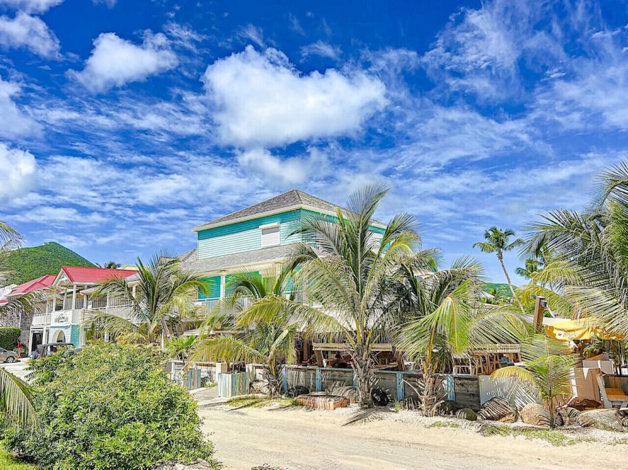 A beachfront property with a large house, palm trees, and a clear blue sky.