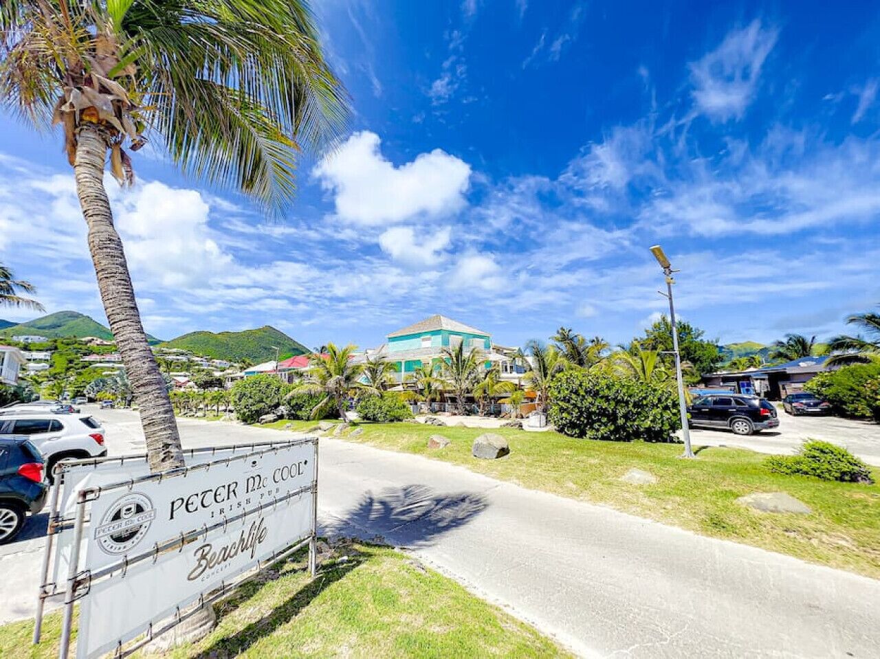 A beachside road with a sign for 'Peter McCoole Irish Pub' and a building in the background.