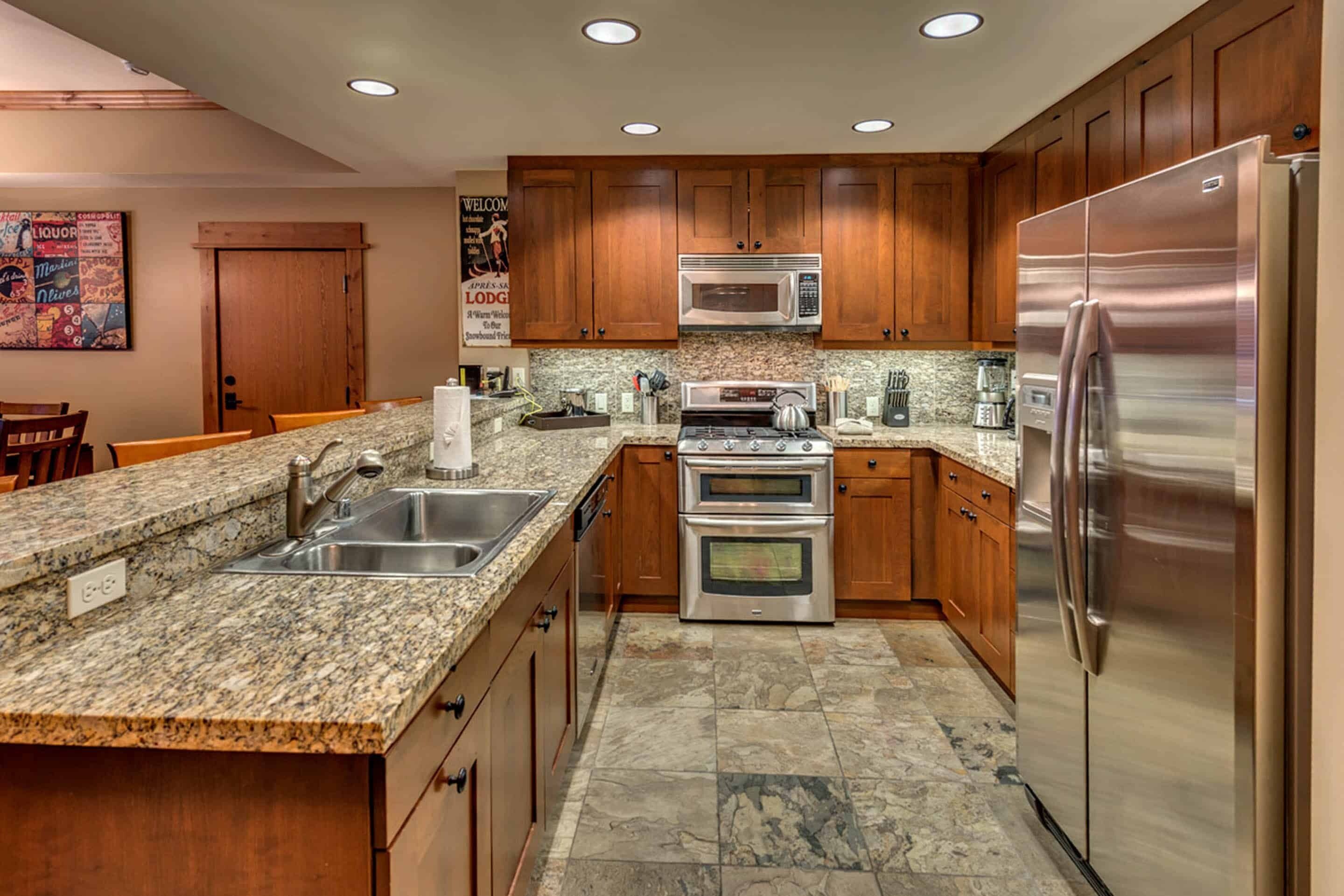 A kitchen with granite countertops, wooden cabinets, stainless steel appliances, and a granite backsplash.
