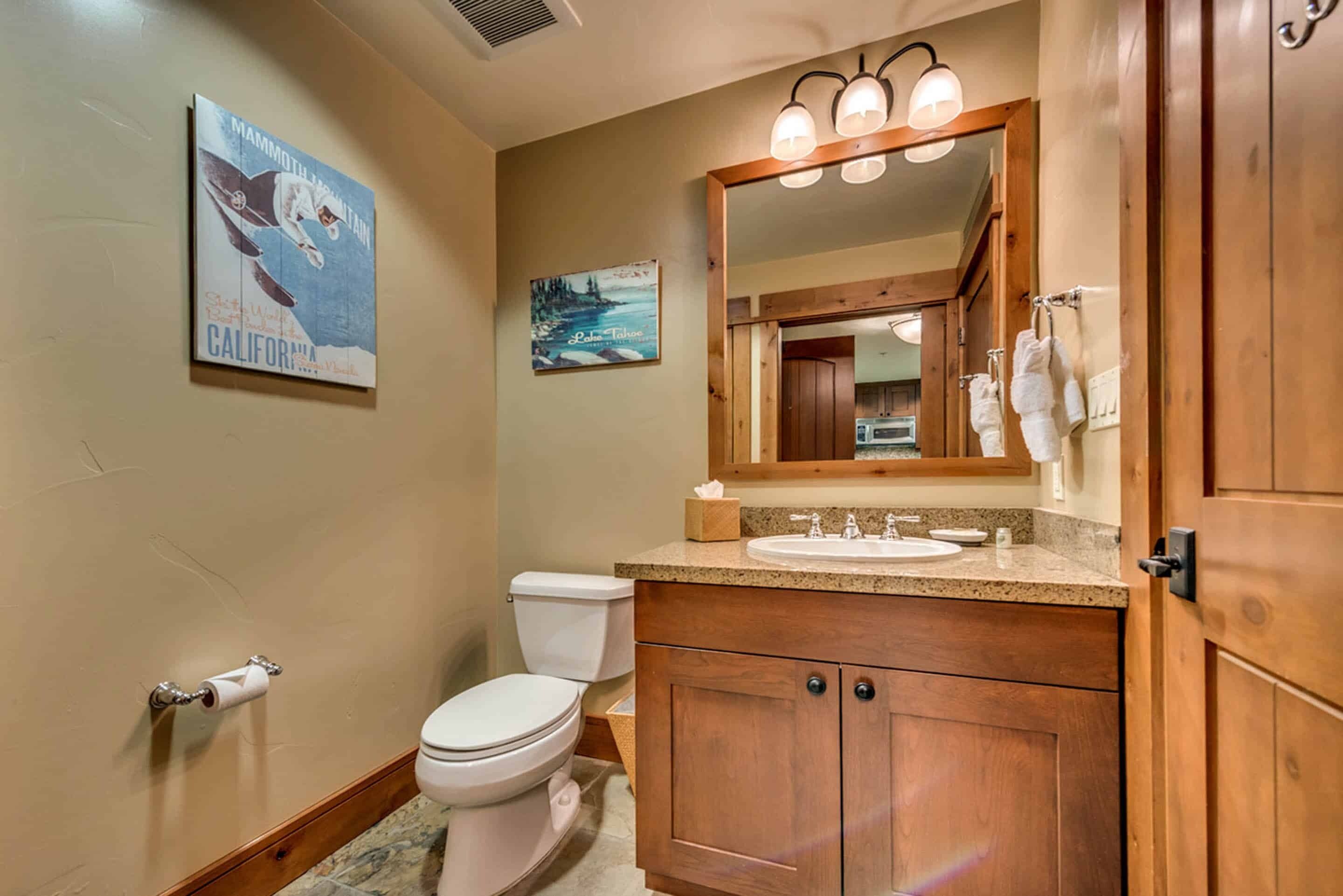 A bathroom with a toilet, sink, wooden cabinets, a mirror, and a poster on the wall.