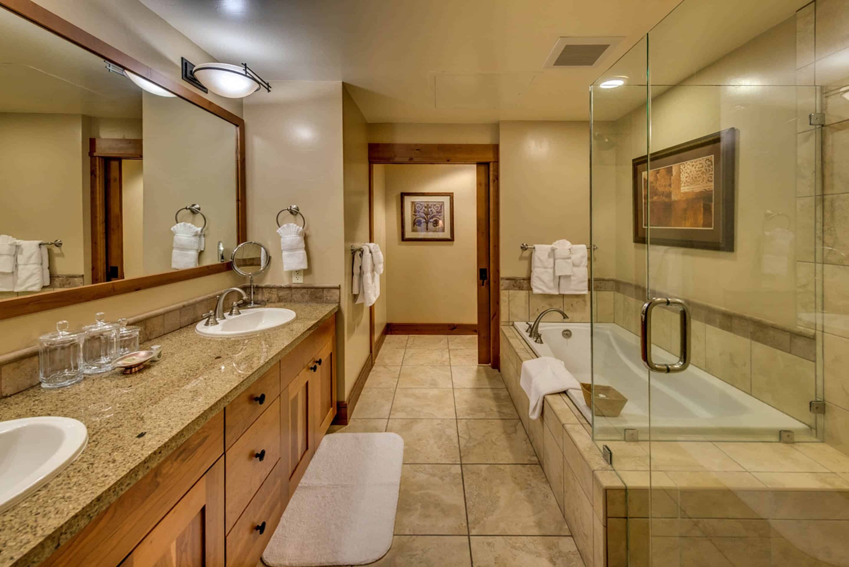 Une salle de bain moderne avec deux lavabos, un grand miroir, une douche à parois de verre et un banc.