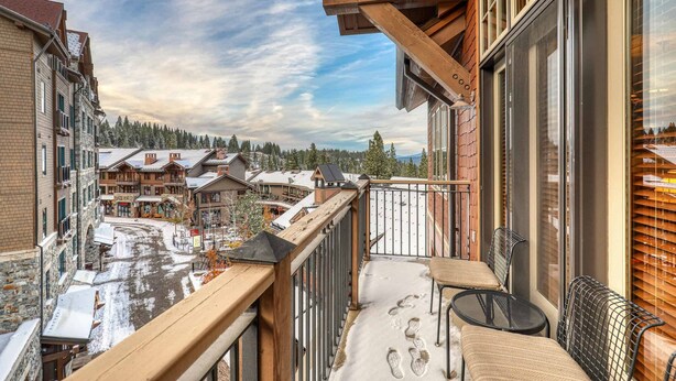 A balcony with a wooden railing, a table, and a chair. - Catamount Lodge 404 Two Bedroom (Truckee)