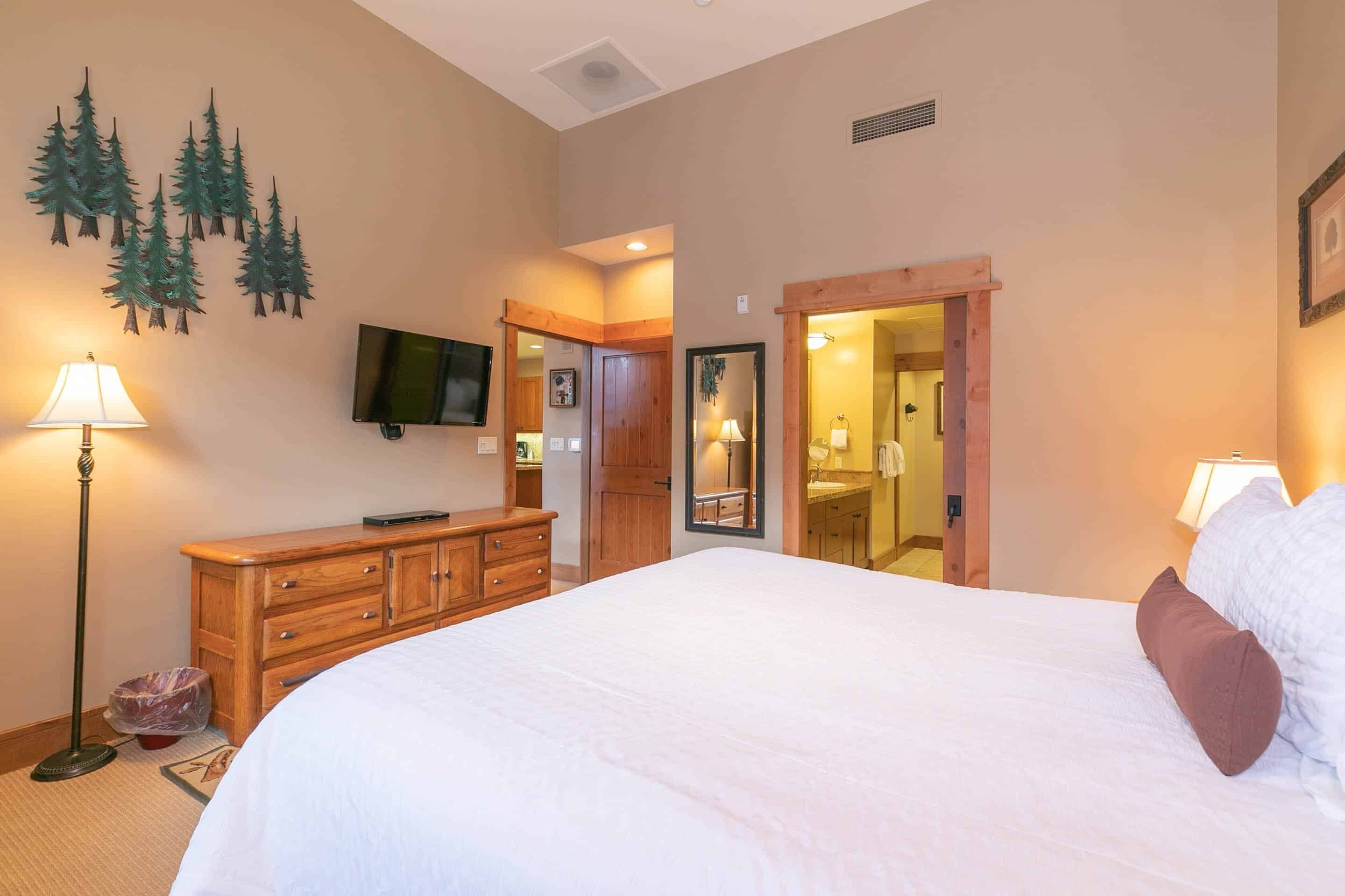 A bedroom with a large bed, wooden dresser, and a television on the wall.