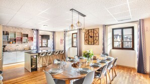 A modern kitchen with wooden cabinets, a central island, and bar stools. A dining area with a wooden table and chairs is adjacent to the kitchen.