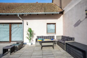 Um pátio externo com sofá, duas cadeiras, uma mesa e um vaso de planta.