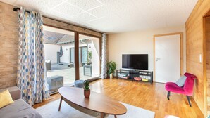 A modern living room with a wooden floor, a sofa, a coffee table, a TV, and a pink chair.