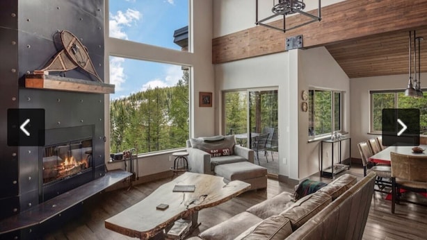 A spacious living area with a fireplace, large windows, a dining area, and a view of the outdoors. - Ski-in/out Mod/Indust Luxe Schweitzer Mountain (Sandpoint)
