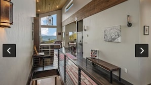 A spacious interior with a high ceiling, a staircase leading to a balcony, and a view of mountains. - Ski-in/out Mod/Indust Luxe Schweitzer Mountain (Sandpoint)
