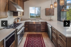 A kitchen with wooden cabinets, a stainless steel stove, and a large window with a view of trees and mountains.