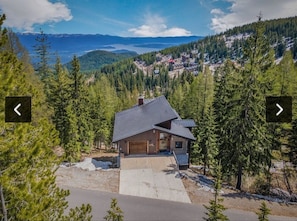 A modern house with a garage, surrounded by a forest and a lake in the background.