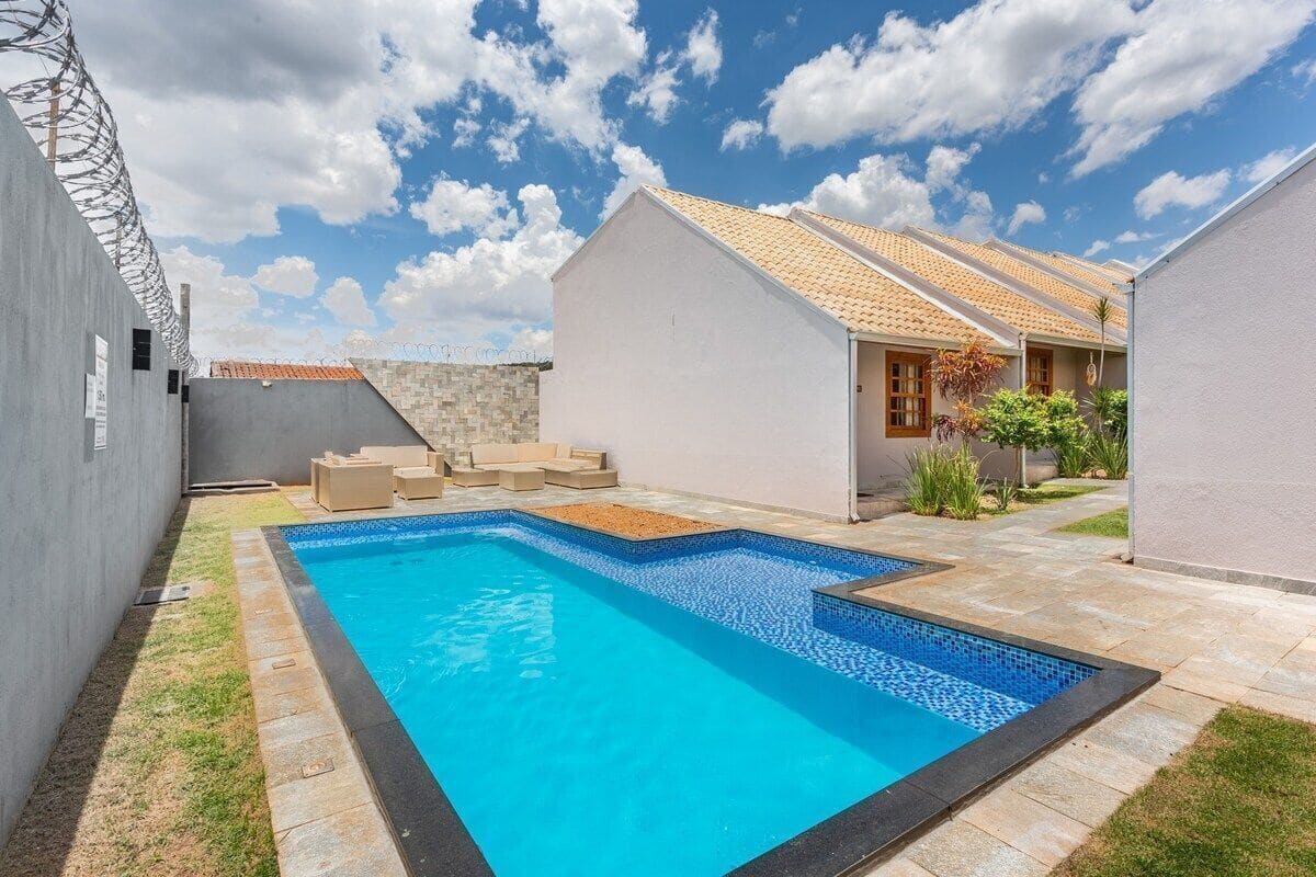 Una piscina con borde de azulejos, rodeada de un patio empedrado y un pequeño jardín.