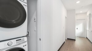 Un lavadero con lavadoras y secadoras apiladas, una pared blanca y piso de madera.