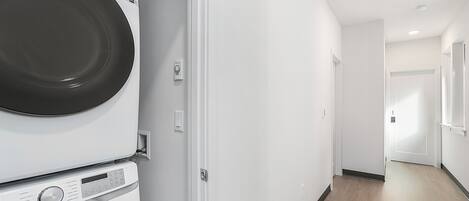 Ett tvättrum med staplade tvättmaskiner och torktumlare, en vit vägg och ett trägolv.