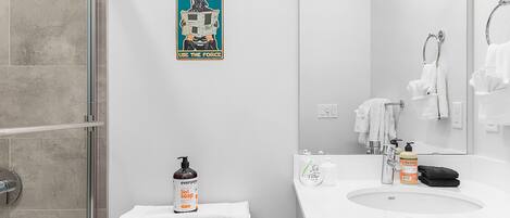 A bathroom with a shower, toilet, sink, and a poster on the wall.