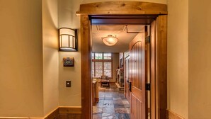 A hallway with a wooden door, a stone-tiled floor, and a light fixture on the wall. - Catamount Lodge 103 Two Bedroom (Truckee)